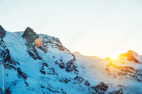 Beautiful nature landscape of Matterhorn mountain peak, Swiss Alps in sunlight rays. Sunset mountains covered with snow in Switzerland. View of Alpine ski resort and sun beams. Winter background.