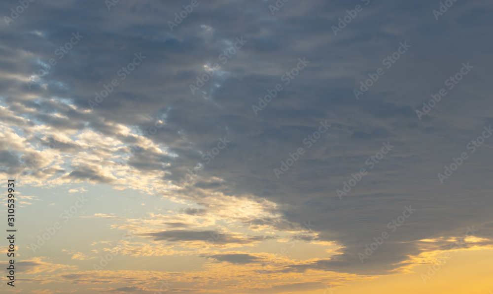 Rows of flattened small clouds float slowly across the sky, illuminated by the yellow rays of the setting sun