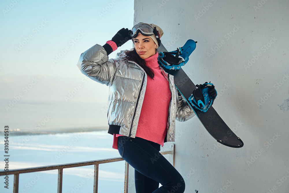 Young active woman with snowboard is posing for photographer at bright winter day.