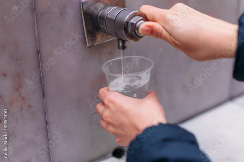 Drinking gallery of mineral spring. close - up of young woman gaining glass of mineral water from tap