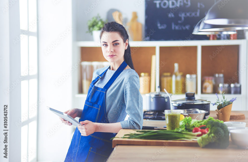 Fototapeta premium Young woman using a tablet computer to cook in her kitchen