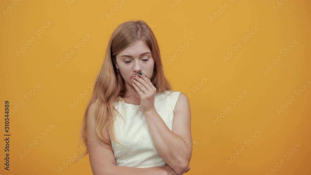 Attractive blonde young woman covering mouth with hand, holding hand on head looking scared over isolated orange background wearing white shirt. Lifestyle concept Attractive blonde young woman covering mouth with hand, holding hand on head looking scared over isolated orange background wearing white shirt. Lifestyle concept
