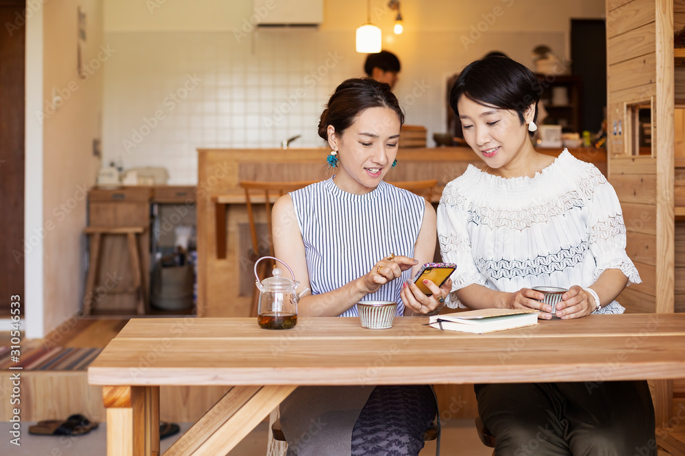 Two Japanese women sitting at a table in a vegetarian cafe, using mobile phone. Two Japanese women sitting at a table in a vegetarian cafe, using mobile phone.