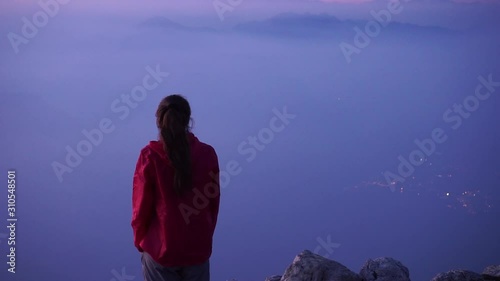 Silhouette Girl female hiker watching an amazing sunset from the top of a mountain in the Dolomiti, Italy, lake Garda. Monte Altissimo. Peaks of the dolomities and lights of the city in the distance photo