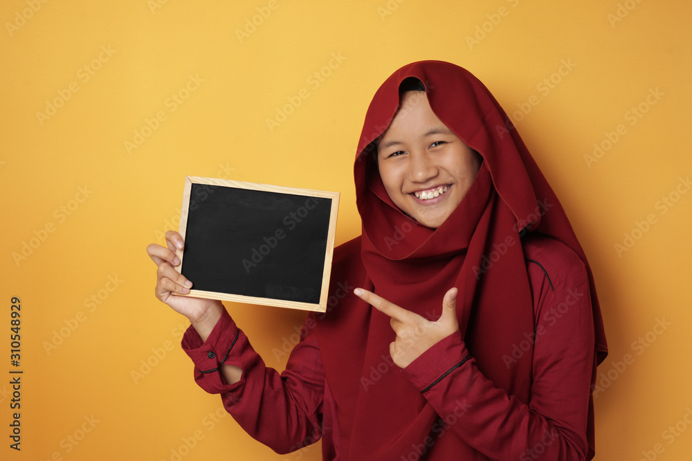 Smart Asian Muslim Teenage Girl Smiling at Camera and Showing Empty Blackboard Smart Asian Muslim Teenage Girl Smiling at Camera and Showing Empty Blackboard