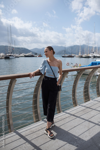 Young tourist woman on a bridge. Woman looks dreamy on the port with ships. Seascape with mountains. Summer vacation in Marmaris, Turkey. Copy space.