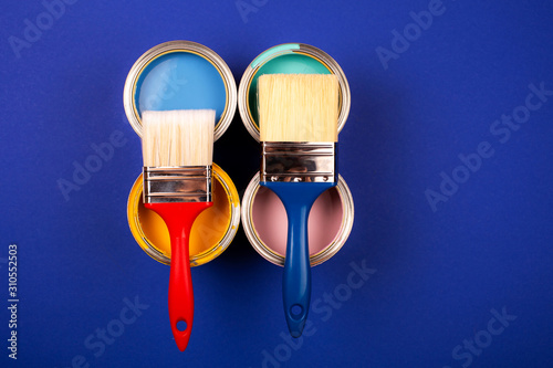 Fototapeta Naklejka Na Ścianę i Meble -  Four open cans of paint with brushes on blue background. Yellow, blue, pink, turquoise colors of paint. Top view.