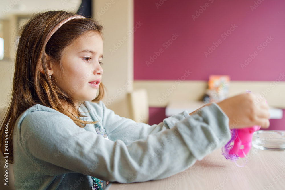 Small girl young caucasian child playing with her toy while sitting at the table in front of purple wall Small girl young caucasian child playing with her toy while sitting at the table in front of purple wall