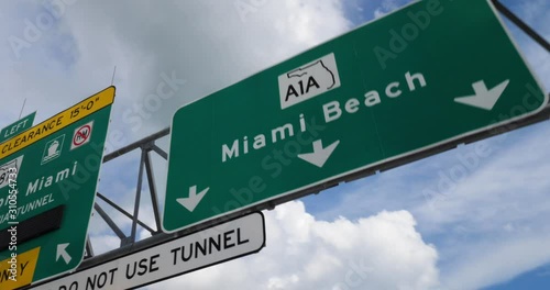 A view driving under a Miami road sign on a sunny day. Miami Beach A1A North and Port Miami via Tunnel and Route 887 are shown.  	 photo