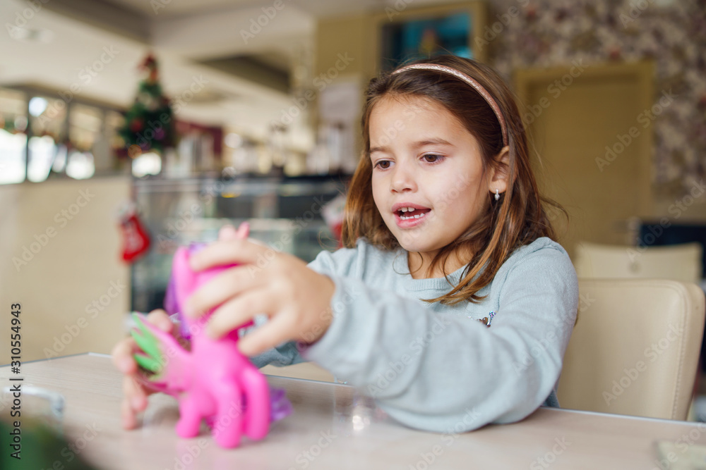 Small girl young caucasian child playing with her toy while sitting at the table at the restaurant cafe or kindergarten Small girl young caucasian child playing with her toy while sitting at the table at the restaurant cafe or kindergarten
