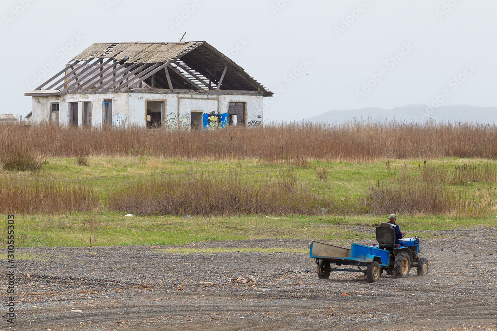 A man rides a tricycle with a cart on the background of an abandoned village house