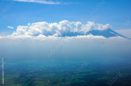 Aerial shot of Mount Rinjani, surround by clouds and an view of residency and agriculture area of Lombok Island, Indonesia.