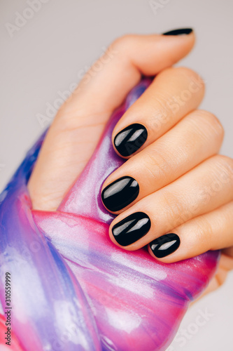 hands with black manicure holding slime in blue and pink vibrant colors