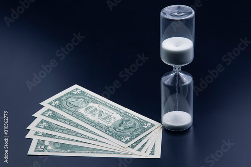 Dollar bills lie near the hourglass. Time is money. The salary. Business solutions in time. Hourglass time measurement