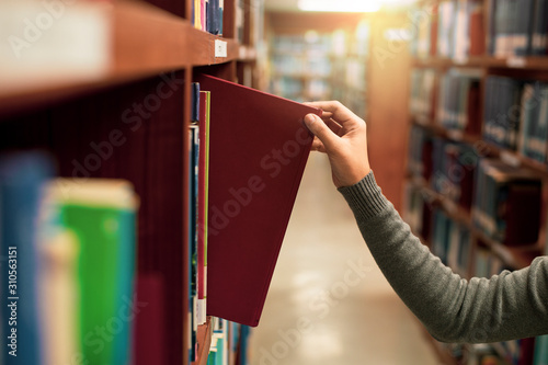 Asia female Hand  picking book from bookshelf at library university,a concept of learning and choice photo