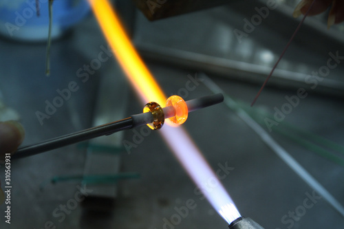 Artist of glass at work. Hand made glass beads in the fire out of red hot glowing glass for pandora bracelets,focus glass bead around blurry