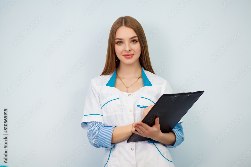 Photo of a young woman doctor posing isolated over white wall background holding clipboard. Health care concept. Beautiful girl in a white coat. Copy space. Photo of a young woman doctor posing isolated over white wall background holding clipboard. Health care concept. Beautiful girl in a white coat. Copy space.