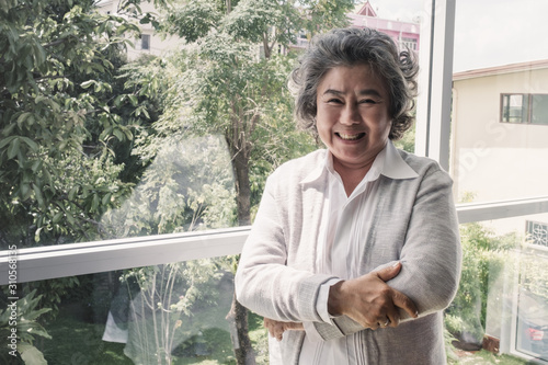Portrait of elderly Asian woman with grey hair smiling and happy standing near window, lifestyle concept