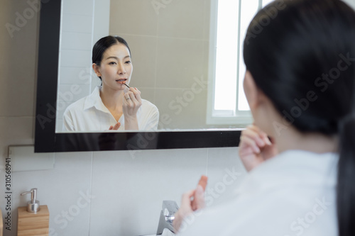 Asian woman wearing white shirt and make up face in front of mirror in bathroom