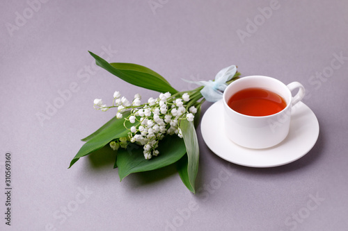 Lily of the valley flowers with green leaves ant teacup on gray background. Flower pattern. Floral background. Top view. Flat lay. Spring, summer concept. March 8, mother's day