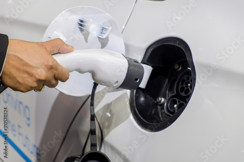 Close-up hand of businessman who holding a rechargeable machine plug for charger battery on socket of white electric car, Electric power is an alternative fuel for smart vehicles, eco energy