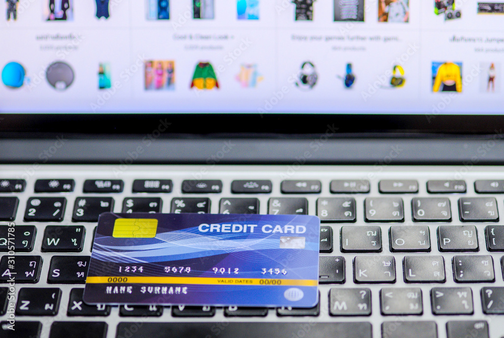 Blue credit card mockup put on keyboard of laptop and blurred web shopping online on display monitor, online shopping and payment via credit card concept