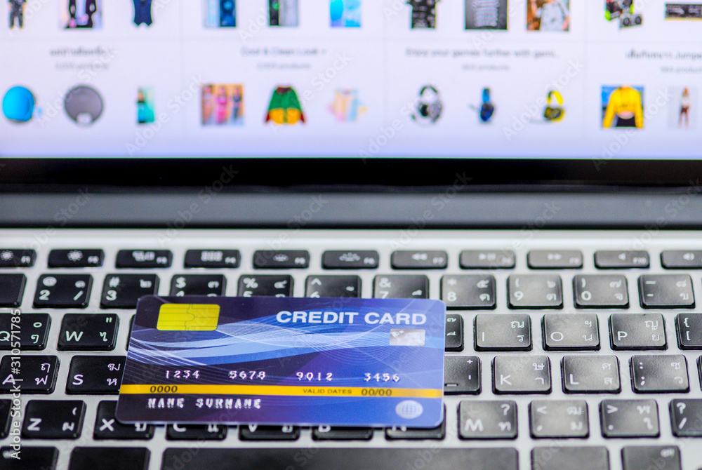 Blue credit card mockup put on keyboard of laptop and blurred web shopping online on display monitor, online shopping and payment via credit card concept Blue credit card mockup put on keyboard of laptop and blurred web shopping online on display monitor, online shopping and payment via credit card concept