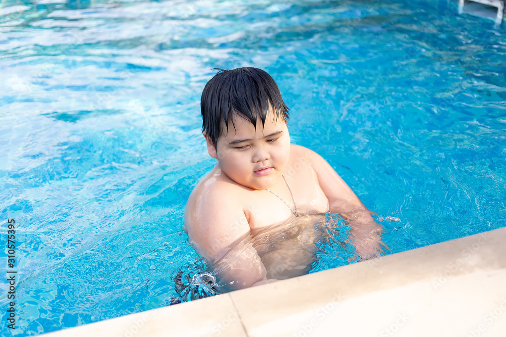 Asian boy is playing in a pool in Thailand.An obese boy swimming in the pool Asian boy is playing in a pool in Thailand.An obese boy swimming in the pool