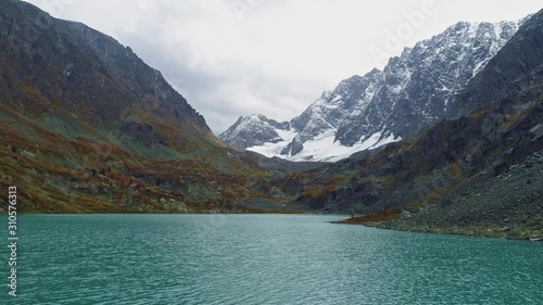 Drone slide over scree shore above ripple turquoise water of alpine Kuyguk lake photo