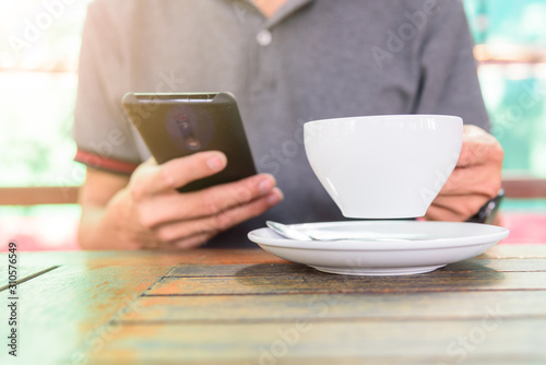 The man use smartphone and take hot coffee for drink