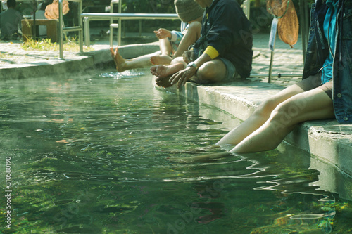 Women and people stretch their legs and feet soaked in hot mineral spring water. Health and relaxation activities at Sankampang Hot Springs, Chiang Mai, Thailand