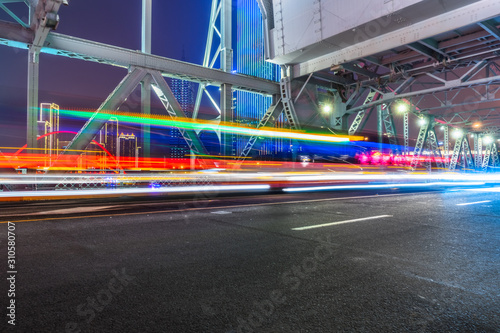 car light trails on steel bridge with city skyline.