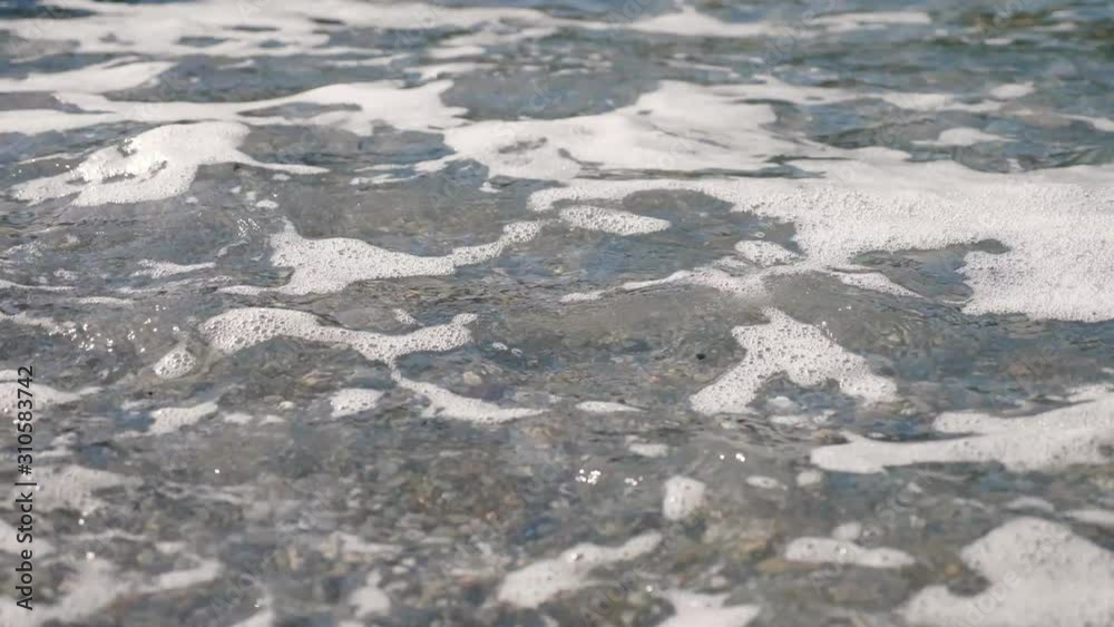 Close-up . soft waves, with white foam are washed ashore, on pebble beach. beautiful , multi-colored round sea pebbles on Mediterranean sea coast, shore. summer hot day. Greece Close-up . soft waves, with white foam are washed ashore, on pebble beach. beautiful , multi-colored round sea pebbles on Mediterranean sea coast, shore. summer hot day. Greece
