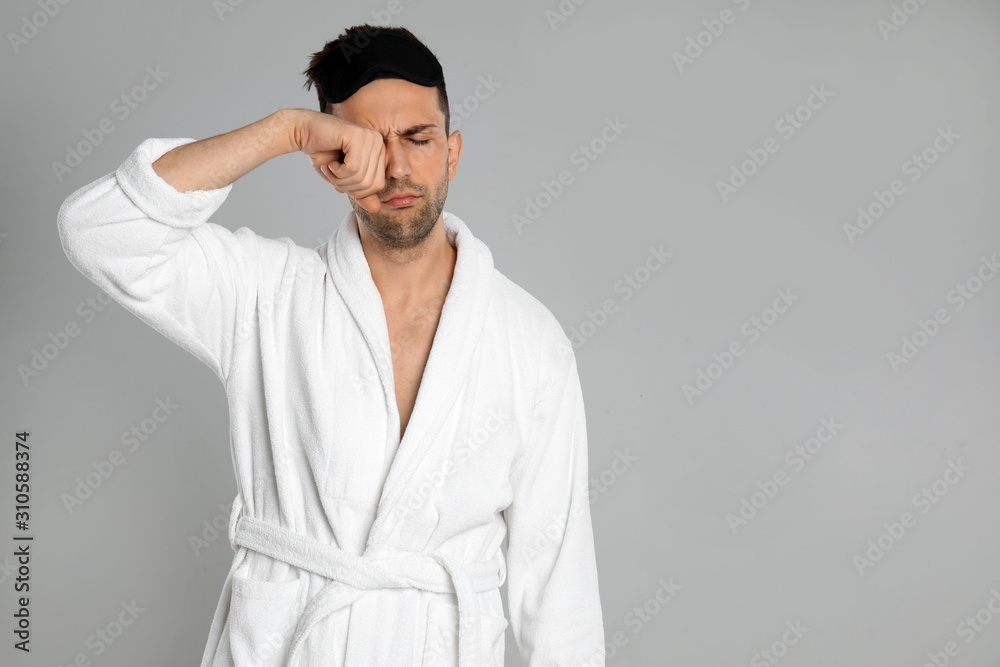 Sleepy young man in bathrobe on light grey background. Space for text