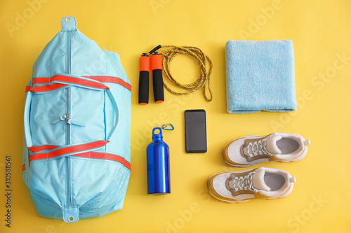 Gym bag  smartphone and sports equipment on yellow background  flat lay