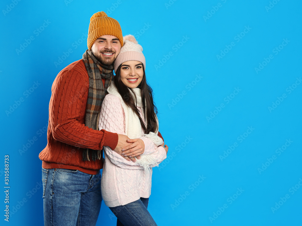 Happy young couple in warm clothes on blue background, space for text. Winter vacation Happy young couple in warm clothes on blue background, space for text. Winter vacation