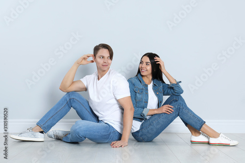 Young couple in stylish jeans sitting near light wall