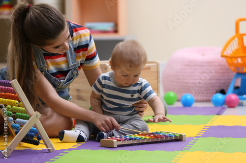 Teen nanny and cute little baby playing with xylophone at home photo