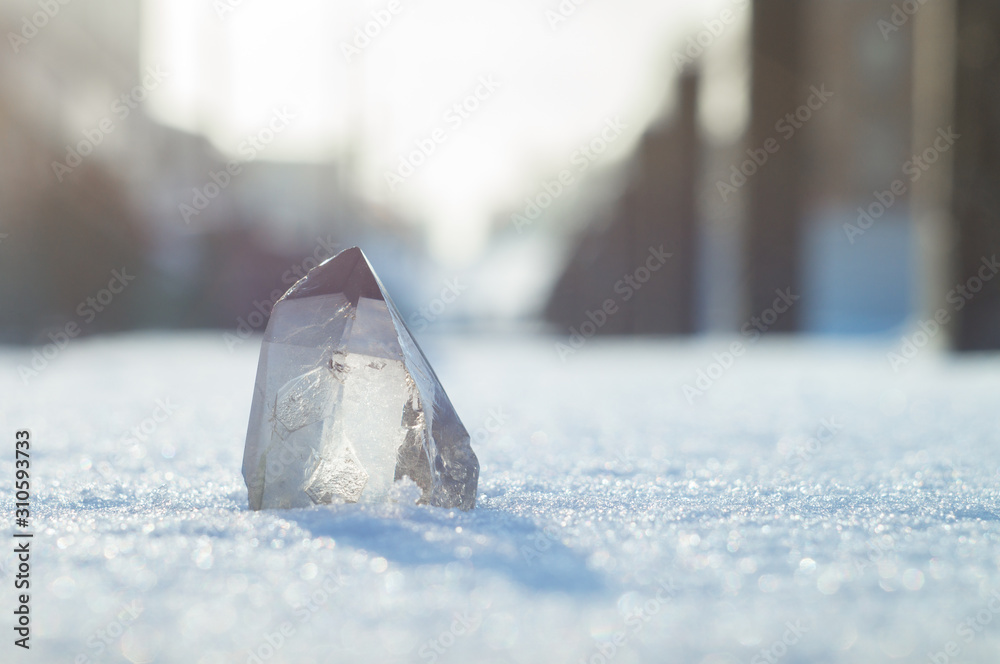Snow-white crystal of pure transparent quartz on snow. Chalcedony contrast on background of blurred city lines - obrazy, fototapety, plakaty 