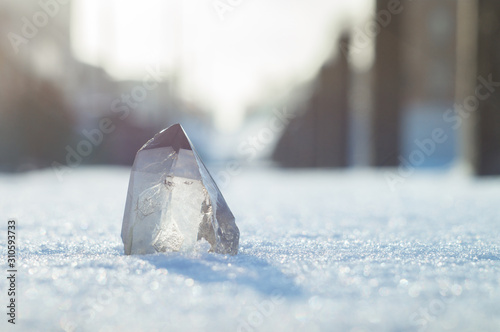 Snow-white crystal of pure transparent quartz on snow. Chalcedony contrast on background of blurred city lines