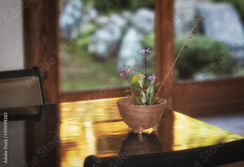 テーブルに飾られた小さな生け花と窓に見える庭園 photo