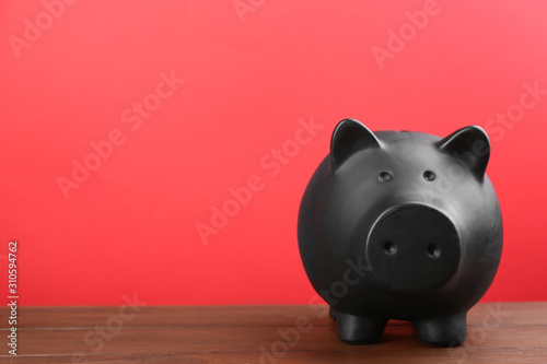 Black piggy bank on wooden table against red background. Space for text