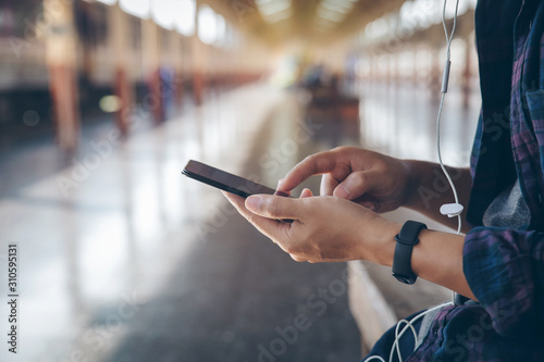 Fototapeta Naklejka Na Ścianę i Meble -  Close-up male hands using smartphone on train station searching or social networks concept, hipster man listen to music on mobile.