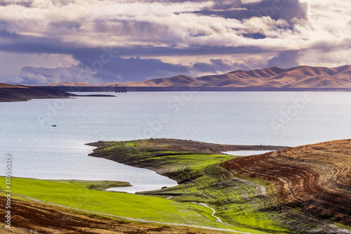 San Luis Reservoir on a stormy day; green grass starting to grow on the shoreline; San Luis Reservoir is a man-made lake storing water for agricultural purposes Merced County, Central California; photo