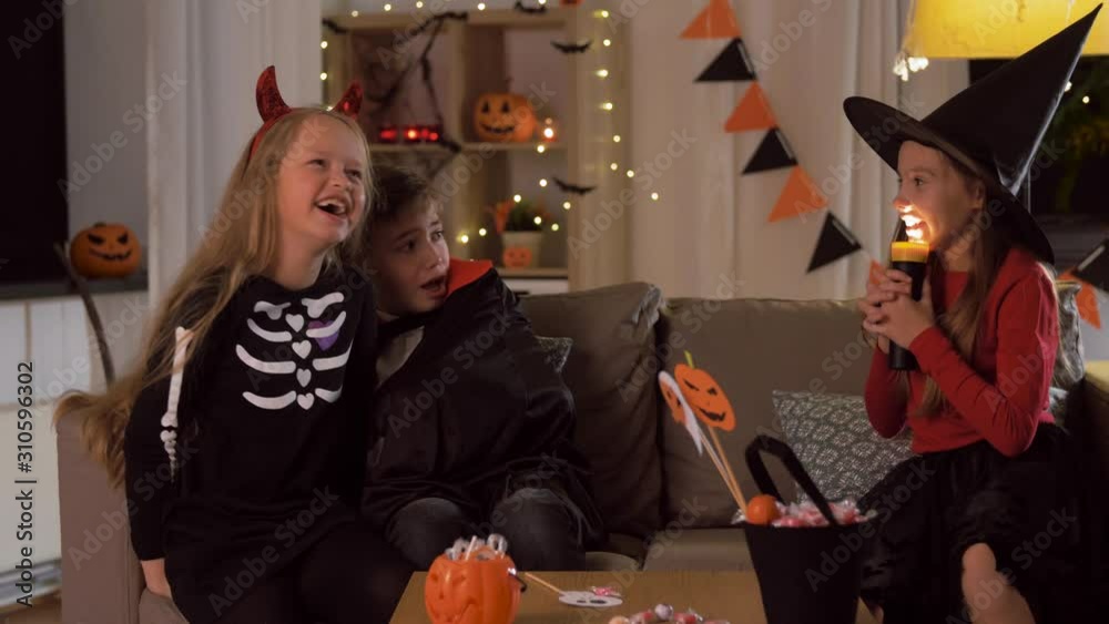 halloween, holiday and childhood concept - smiling boy and girls in costumes playing with flashlight and scaring each other at home