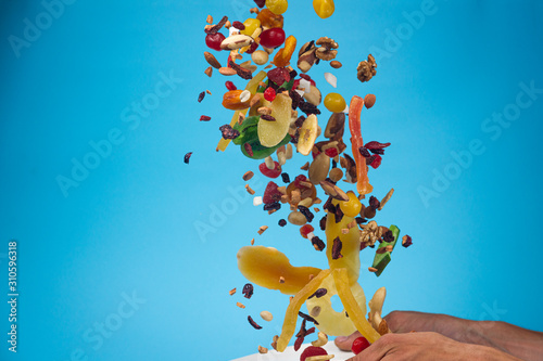 Male hands holding an empty white bowl on blue background. Candied fruits and nuts flying above the bowl.