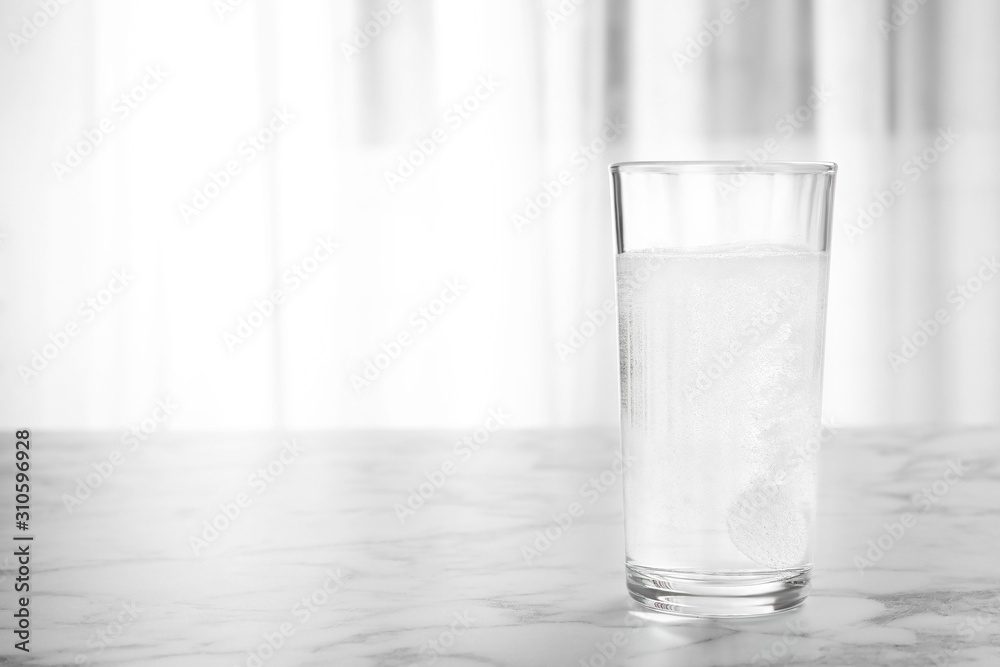 Glass of water with effervescent tablet on marble table indoors, space for text Glass of water with effervescent tablet on marble table indoors, space for text