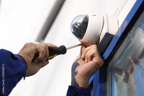 Technician installing CCTV camera on wall outdoors, closeup photo