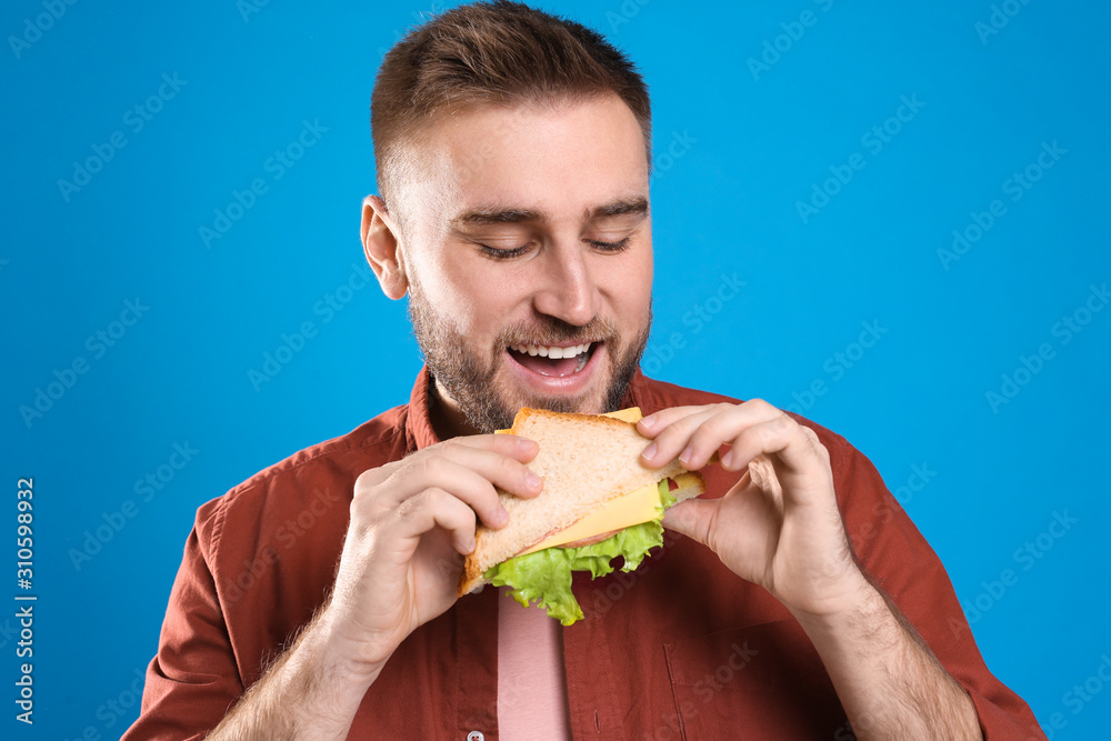 Young man eating tasty sandwich on light blue background