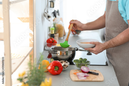 Young man pouring delicious soup into bowl at home  closeup